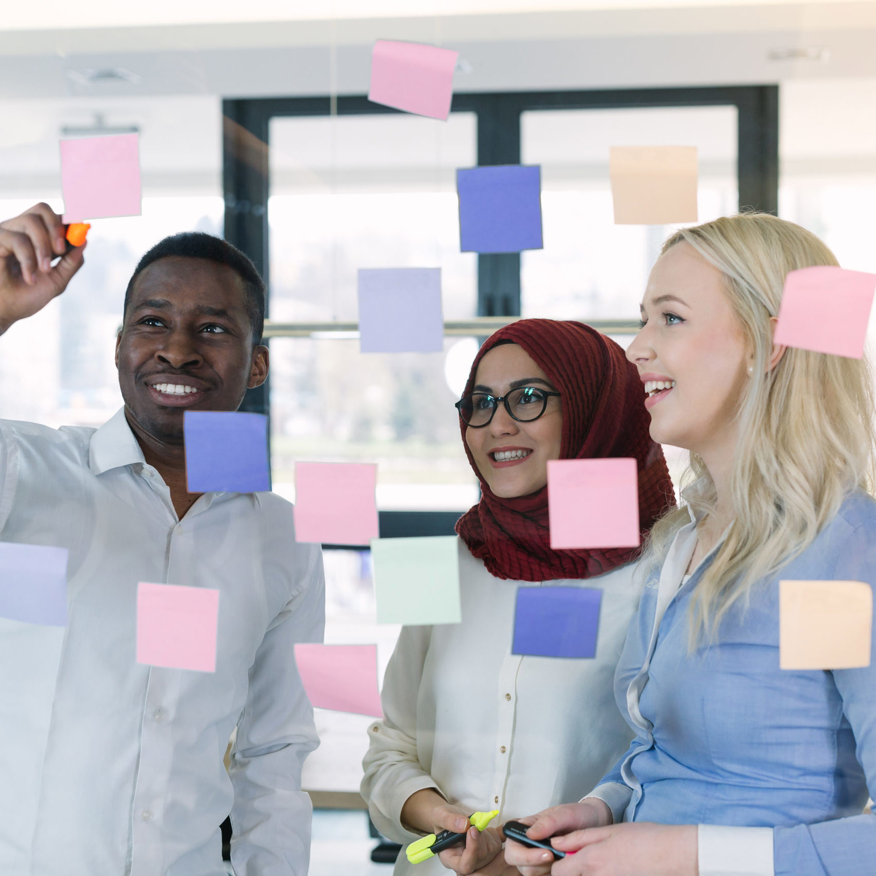 three colleagues studying post it notes on a glass wall