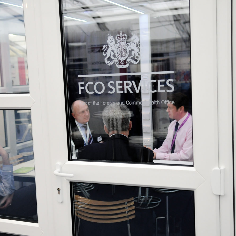 secure room made of glass with FCDO Services logo on and four men sat around table