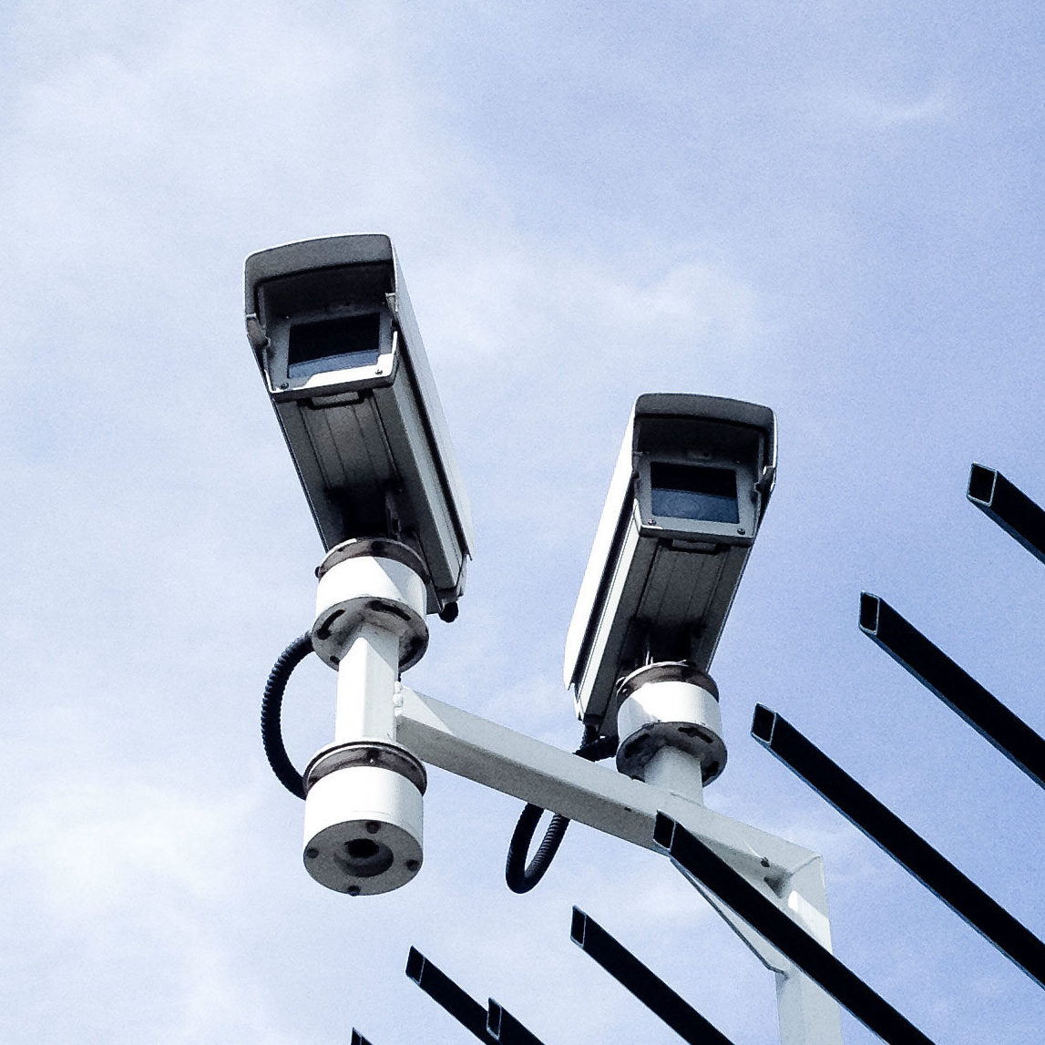 Two cctv cameras mounted on a fence with blue sky