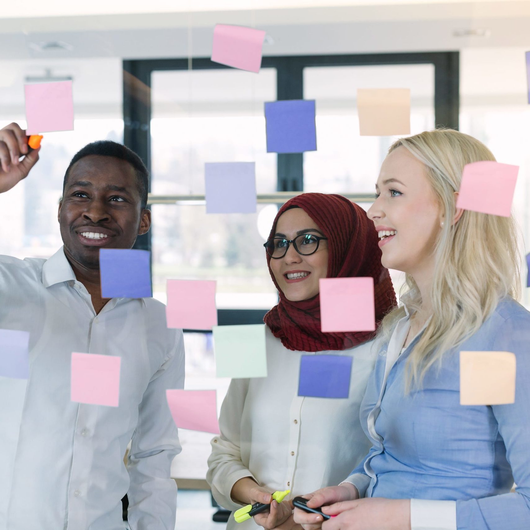 three colleagues looking at post it notes on a glass wall